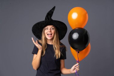 Siyah ve turuncu hava balonlarını tutan genç cadı sürpriz bir yüz ifadesiyle
