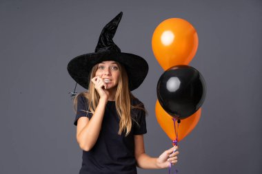 Siyah ve turuncu balonlar tutan genç cadı gergin ve korkmuş.