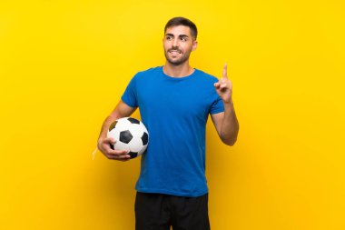 Young handsome football player man over isolated yellow wall intending to realizes the solution while lifting a finger up