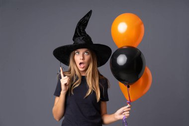 Siyah ve turuncu hava balonları tutan genç cadı işaret parmağıyla işaret ediyor. Harika bir fikir.