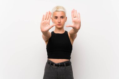 Teenager girl with short hair over white wall making stop gesture and disappointed