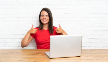 Masada bilgisayarı olan genç bir kız baş parmak hareketi yapıyor.