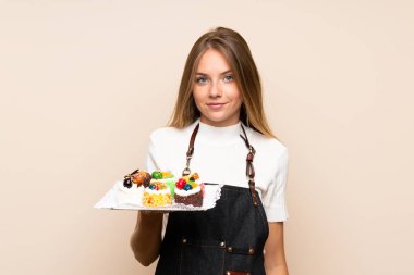 Sarışın bir kadın, izole edilmiş arka planda mini pastalar tutuyor.