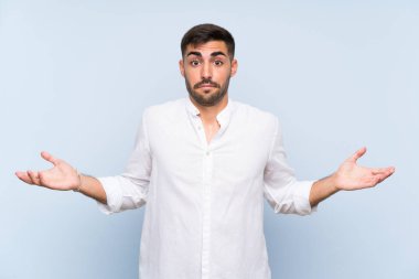 Sakallı yakışıklı, soyutlanmış mavi arkaplan kuşkulu bir jest yapıyor.