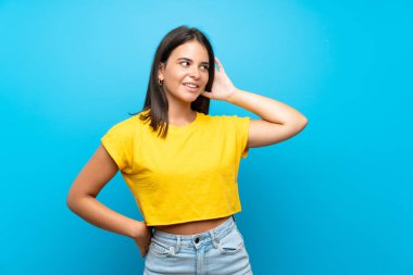 Izole mavi arka plan üzerinde genç kız kulağına el koyarak bir şey dinlerken