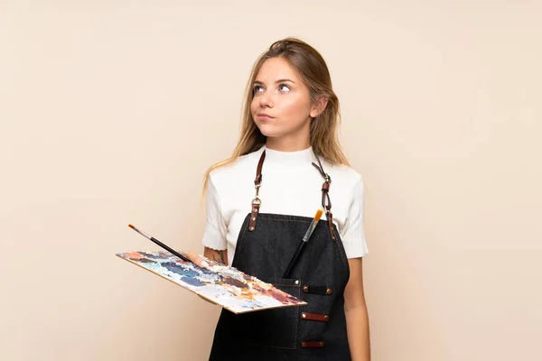 Joven Rubia Sobre Fondo Aislado Sosteniendo Una Paleta Pensando Una — Foto de Stock