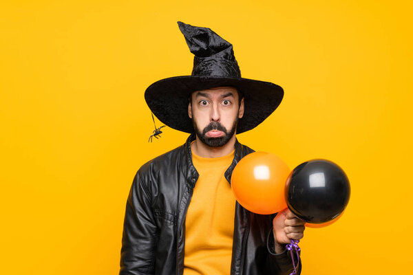 Man with witch hat holding black and orange air balloons for halloween party with sad and depressed expression