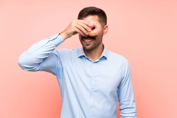 Junger Mann hält einen Donut über isoliertem rosa Hintergrund — Stockfoto