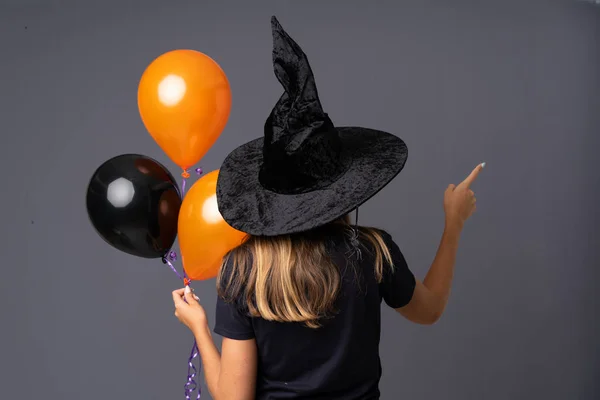 Молодая Ведьма Держит Черные Оранжевые Воздушные Шары Указывая Назад Указательным — стоковое фото