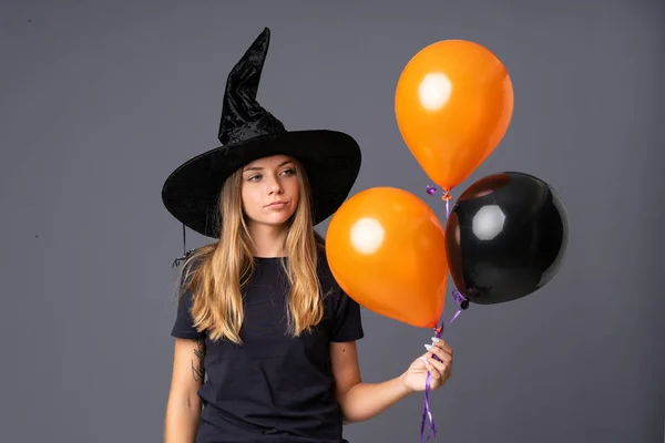Young witch holding black and orange air balloons thinking an idea