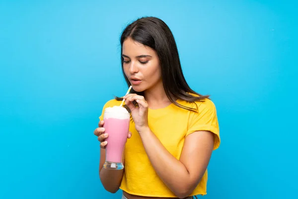 Chica joven con batido de fresa sobre fondo azul aislado —  Fotos de Stock