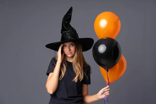 黒とオレンジの気球を保持し 何かに不満を持つ若い魔女 否定的な表情 — ストック写真