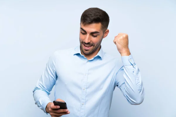 Joven Hombre Guapo Con Móvil Sobre Aislado Muro Azul Celebrando —  Fotos de Stock