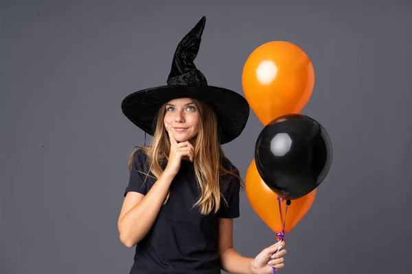 Young witch holding black and orange air balloons thinking an idea