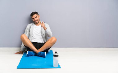 Sport man sitting one the floor points finger at you