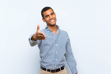 Genç, yakışıklı esmer adam izole edilmiş mavi arka planda iyi bir anlaşma için el sıkışıyor.