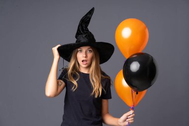 Siyah ve turuncu hava balonlarını tutan genç cadı sürpriz bir yüz ifadesiyle