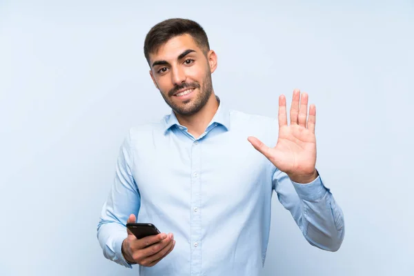 Genç Yakışıklı Adam Cep Telefonuyla Izole Edilmiş Mavi Duvarda Mutlu — Stok fotoğraf