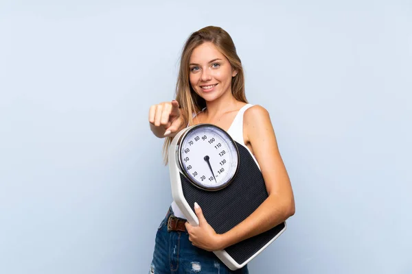 Young blonde girl with weighing machine over isolated blue white — ストック写真