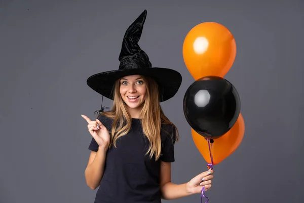 年轻的女巫拿着黑色和橙色的气球 手指指向旁边 — 图库照片