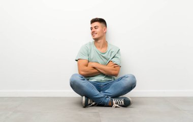Genç yakışıklı adam yerde oturuyor, yan tarafa bakıyor.