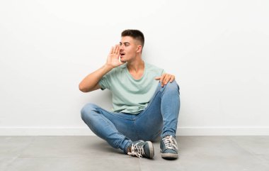 Genç yakışıklı adam yerde oturuyor ve ağzı açık bağırıyor.