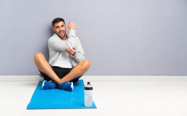 Spor adamı yerde oturuyor ve güçlü bir jest yapıyor.