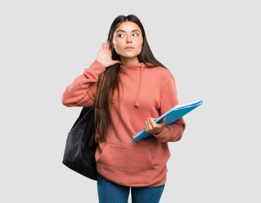 İzole gri arka plan üzerinde kulağına el koyarak bir şey dinleyerek dizüstü tutan genç öğrenci kadın