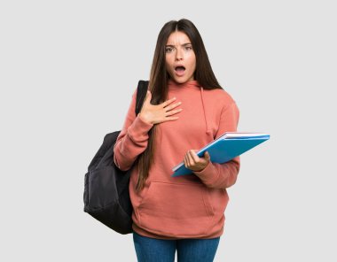 Tecrit edilmiş gri arka plana bakarken defter tutan genç öğrenci kadın şaşırmış ve şok emiş