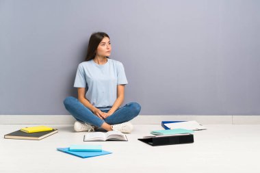 Yerde bir sürü kitabı olan genç bir bayan öğrenci.