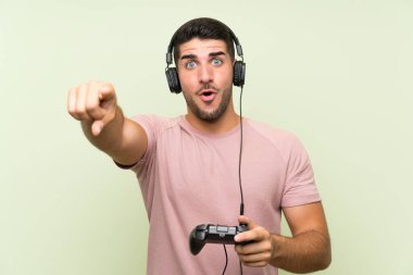Genç yakışıklı adam izole yeşil duvar üzerinde bir video oyunu denetleyicisi ile oynarken şaşırttı ve ön işaret