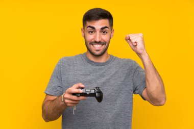 İzole sarı arka plan üzerinde bir video oyunu denetleyicisi ile oynayan genç yakışıklı adam