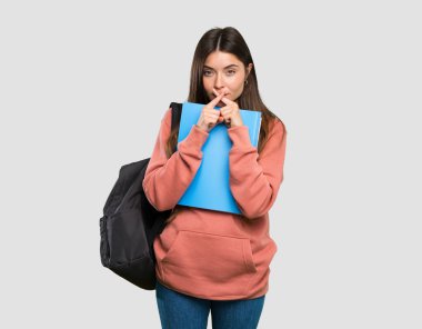 Elinde not defterleri olan genç bir bayan izole edilmiş gri arka planda sessizlik işareti gösteriyor.