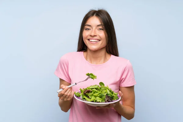 Mujer joven con ensalada sobre fondo azul aislado — Foto de Stock