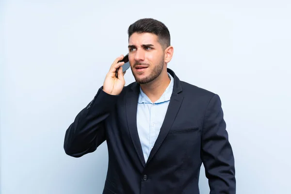 携帯電話との会話を保つ孤立した青い背景の上のハンサムな男 — ストック写真