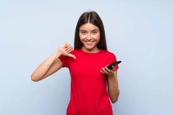 Morena Joven Con Teléfono Móvil Sobre Pared Azul Aislado Orgulloso —  Fotos de Stock