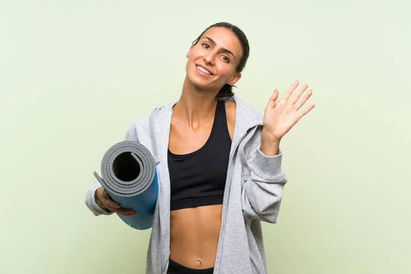 Giovane Donna Sportiva Con Tappetino Sfondo Verde Isolato Saluto Con — Foto Stock