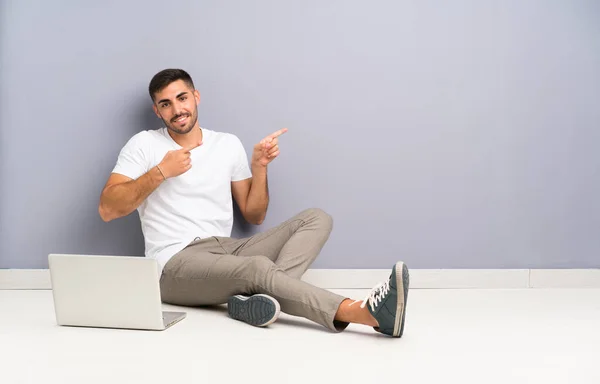 Joven Con Portátil Sentado Suelo Apuntando Con Dedo Hacia Lado — Foto de Stock