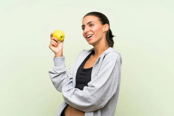 Jonge Sportvrouw met een appel over geïsoleerde groene achtergrond — Stockfoto