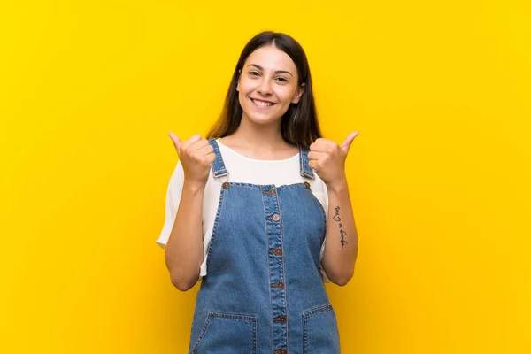 Jonge Vrouw Dungarees Geïsoleerde Gele Achtergrond Met Duimen Omhoog Gebaar — Stockfoto