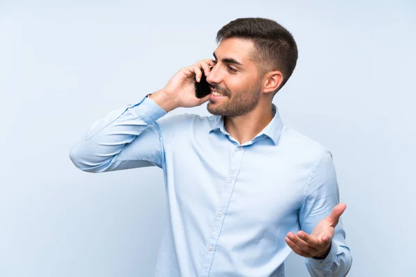 Jeune homme beau avec son mobile sur un mur bleu isolé — Photo