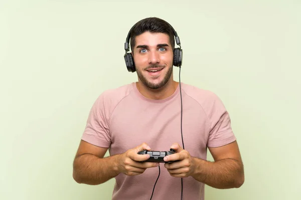 Joven hombre guapo jugando con un controlador de videojuegos sobre una pared verde aislada —  Fotos de Stock