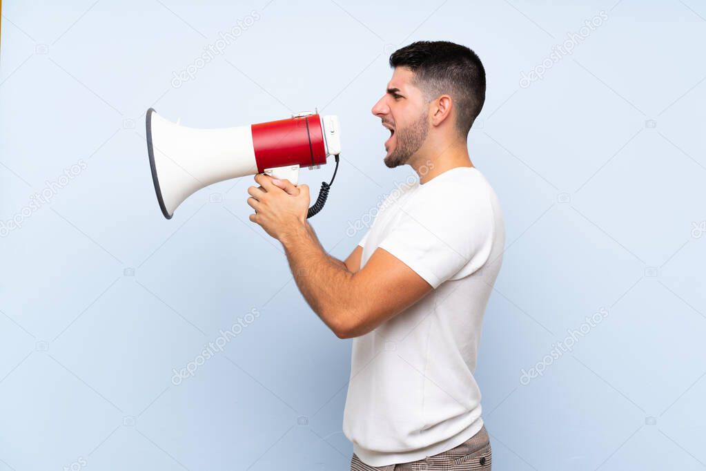 Caucasian handsome man over isolated blue background shouting through a megaphone