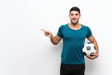 Yakışıklı genç futbolcu, izole edilmiş beyaz duvarın üstünde şaşkın şaşkın ve parmağıyla kenarı işaret ediyor.