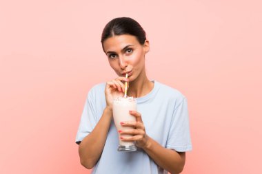 Soyutlanmış pembe arka planda çilekli milkshake ile genç bir kadın.
