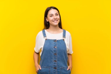 Izole sarı arka plan üzerinde dungarees genç kadın gülüyor
