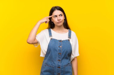 İzole edilmiş sarı arka planı olan genç bir kadın deliliğin jestini yapıyor ve parmağını kafaya koyuyor.