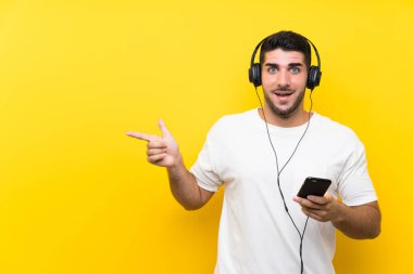 Genç yakışıklı adam müzik dinliyor. Seyyar, izole edilmiş sarı bir duvarı var. Şaşırmış ve parmağıyla işaret ediyor.