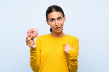 Genç kadın sürpriz yüz ifadesi ile izole mavi arka plan üzerinde bir donut tutan