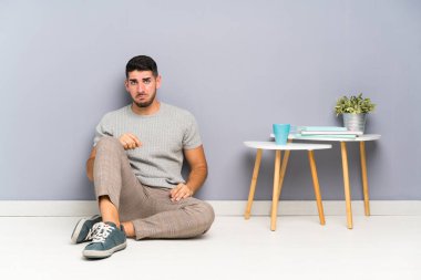 Genç yakışıklı adam üzgün bir şekilde yerde oturuyor.